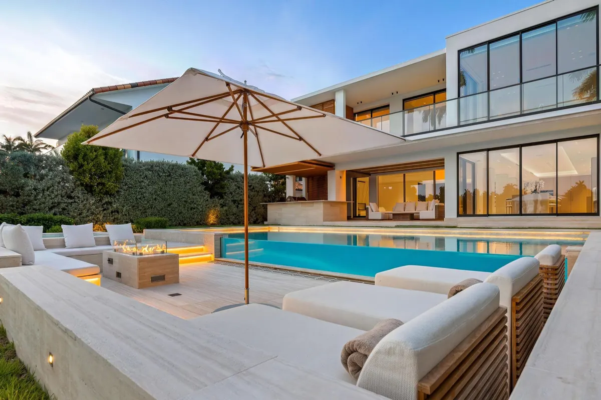 Pool terrace with a white outdoor sofa and large umbrella beside a modern home