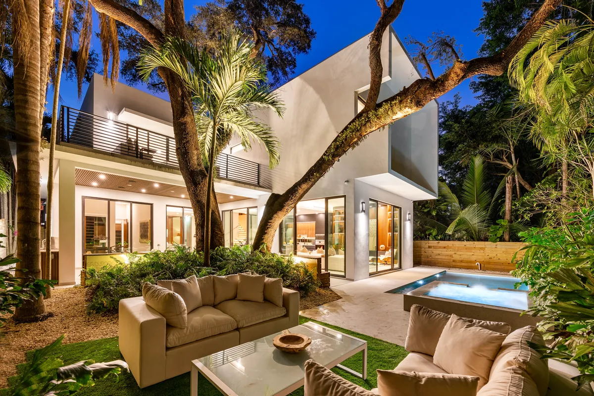 Modern white home around a planted courtyard, outdoor seating and a pool at night