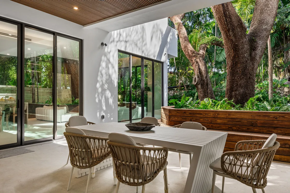 Covered outdoor dining area beside a mature tree and a planted courtyard