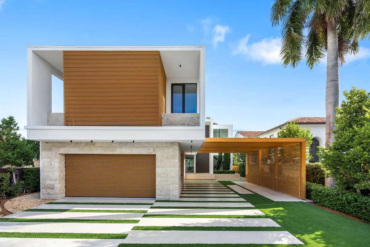 White modern home with wood-clad panels and a striped driveway beneath palms