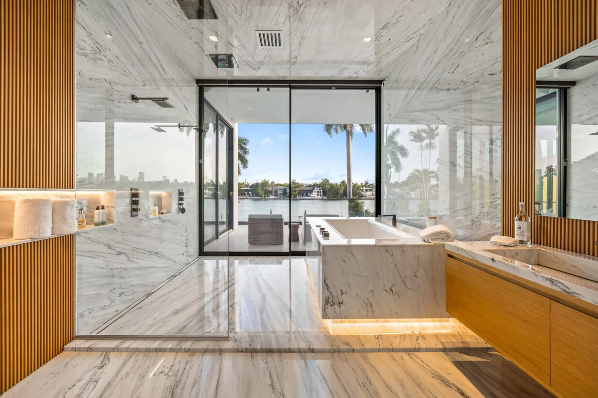 Marble-lined bathroom with a freestanding bath, wood vanity and large waterfront window