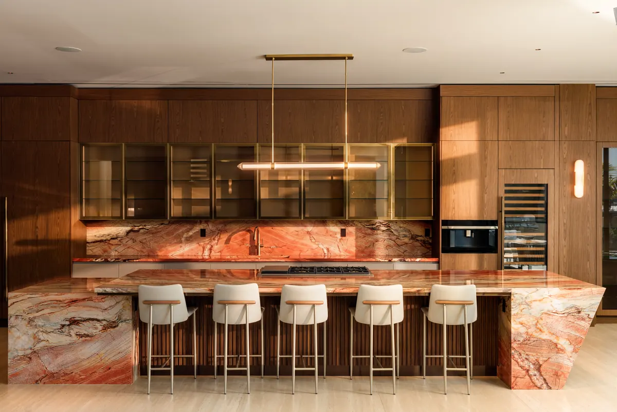 Kitchen with a veined stone island, wood cabinetry and a row of bar stools