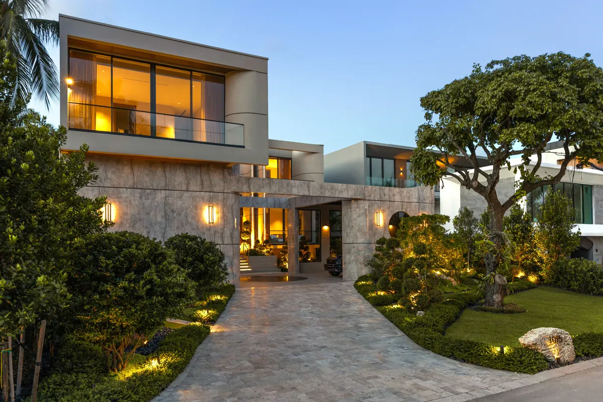 Modern two-story home with illuminated windows and a landscaped driveway at dusk