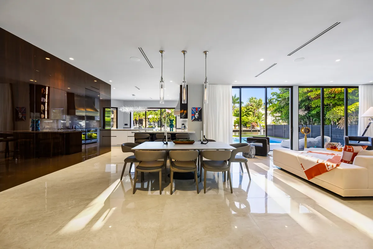 Open kitchen and dining area with pendant lights, dark cabinetry and doors to the pool