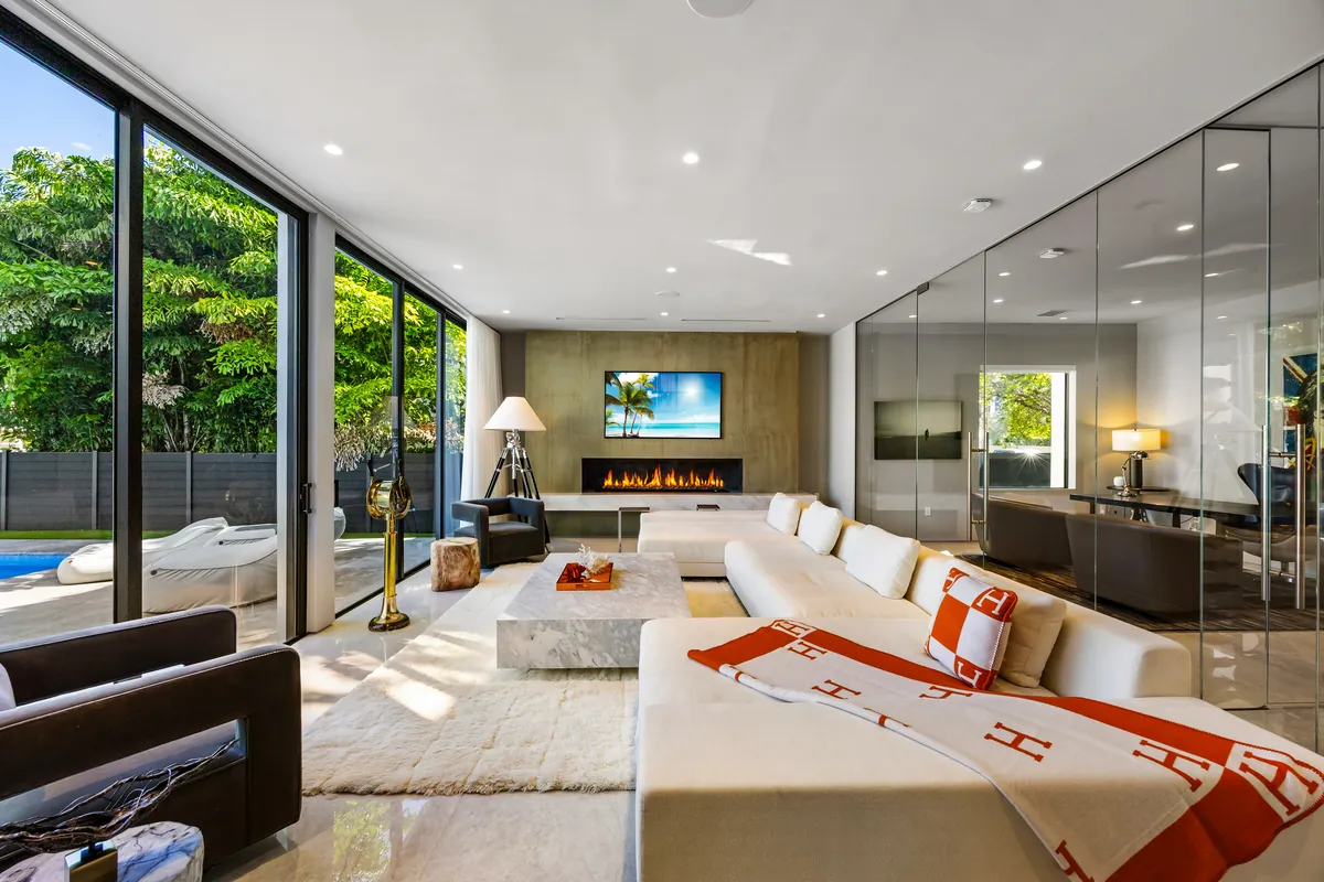 Long living room with pale seating, dark wood cabinetry and full-height garden windows