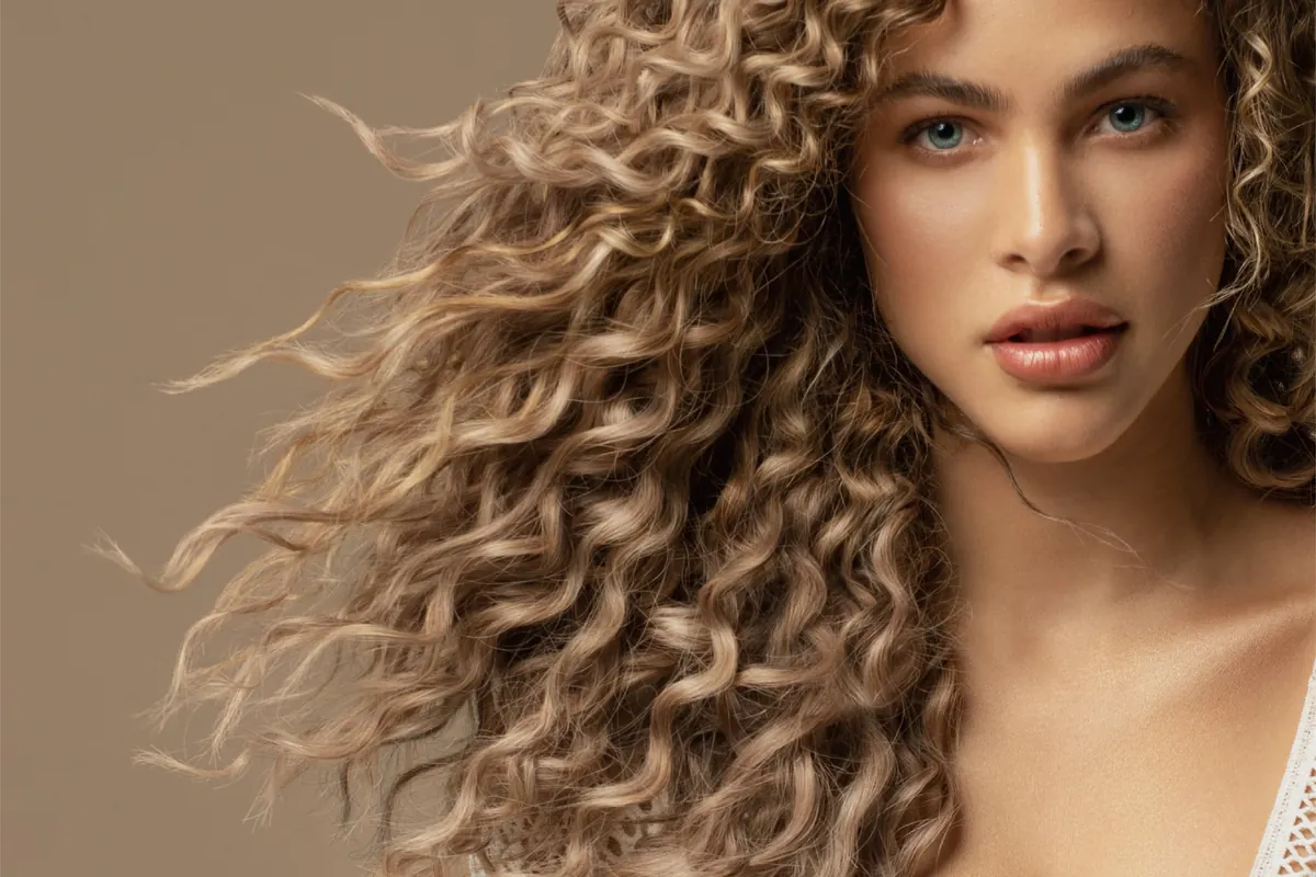 Studio portrait of a woman with curly hair against a warm neutral background
