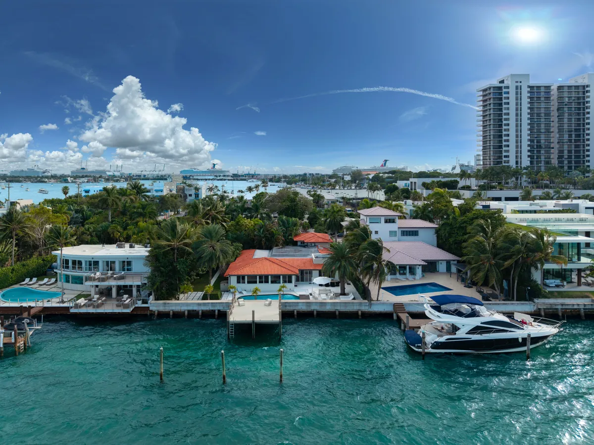 Aerial view of a waterfront home with a red-tiled roof, palms and a wooden dock