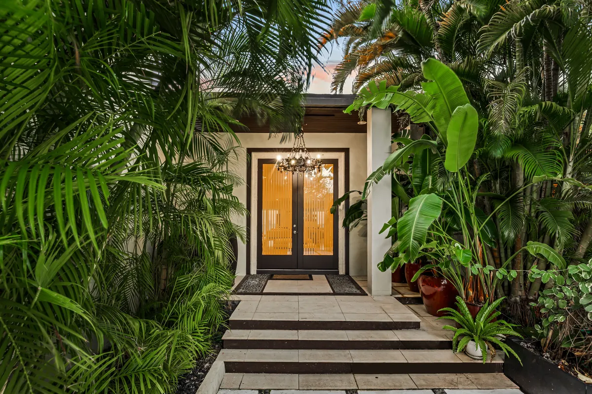 Walkway through dense tropical planting toward a glass entrance door
