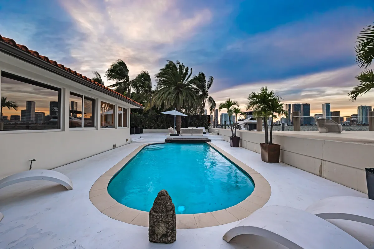 Curved swimming pool beside a covered terrace and palms at dusk